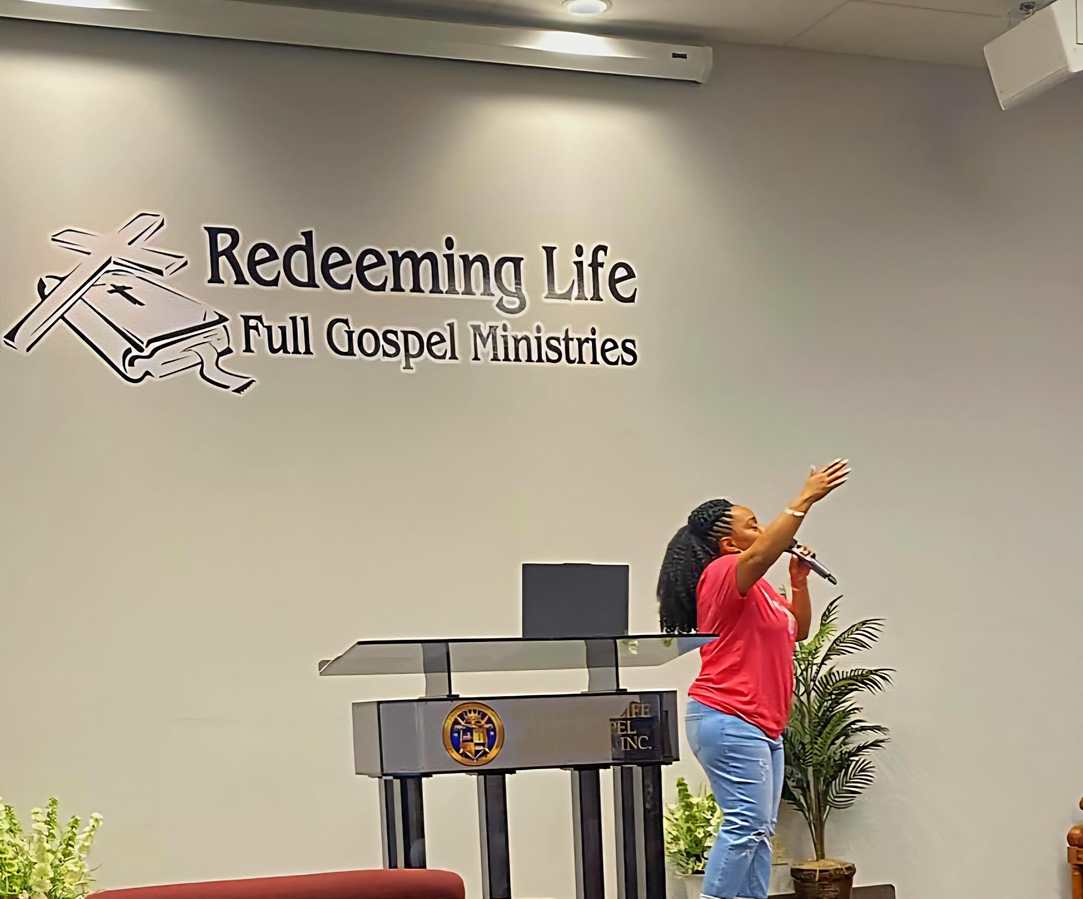 Marsha lifting a hand in worship beneath the Redeeming Life Full Gospel Ministries sign.