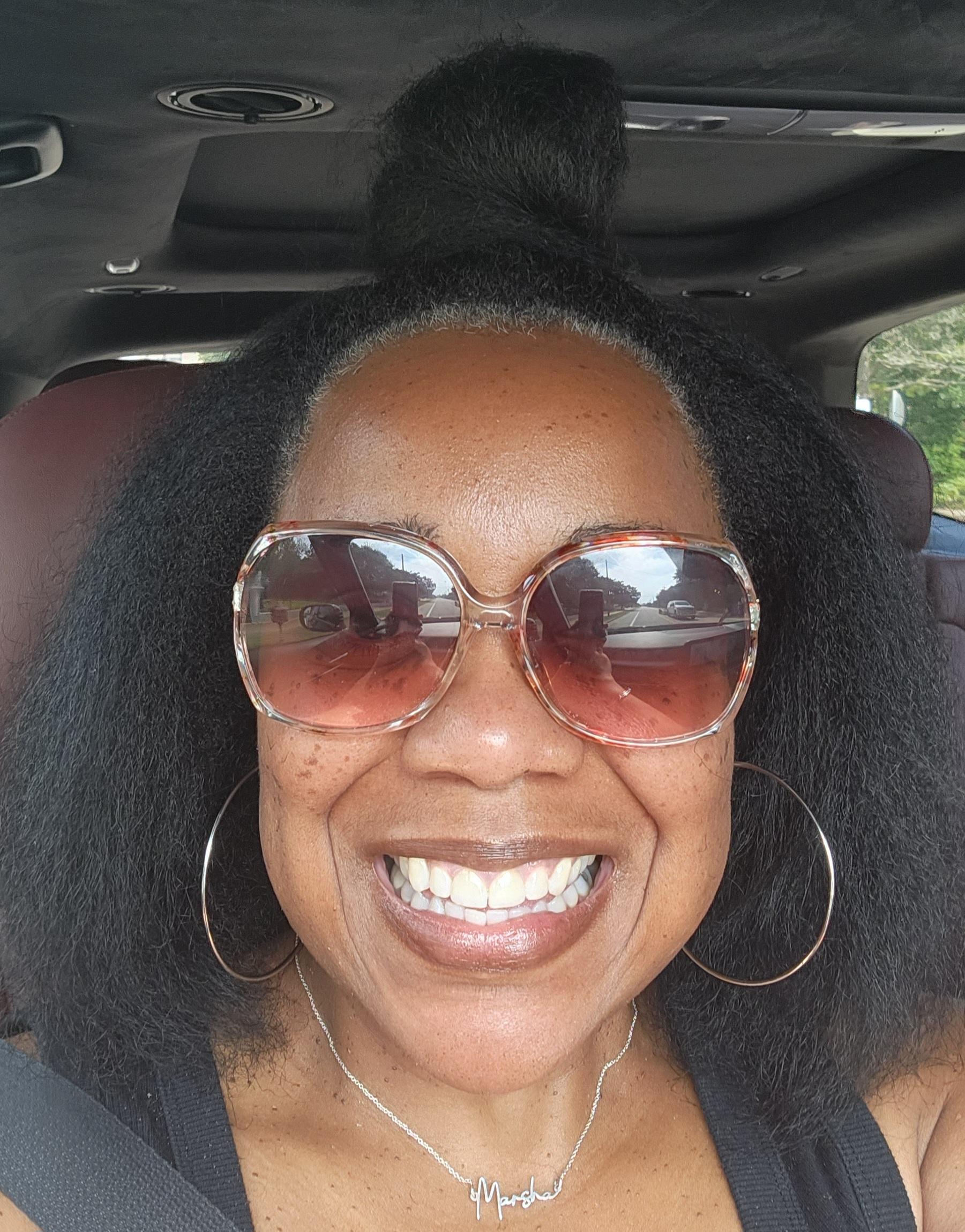 Marsha smiling in sunglasses, wearing her name necklace.