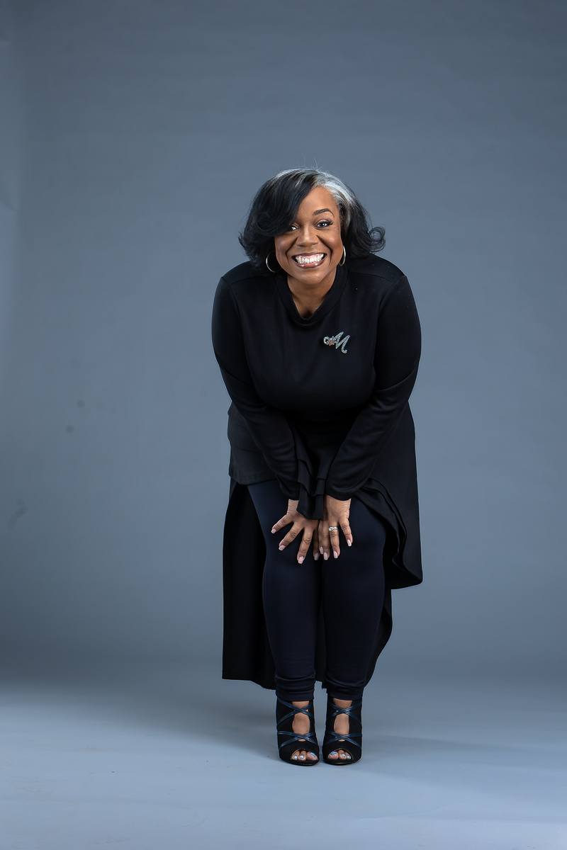 Marsha in all black, leaning forward with a warm smile in the studio.