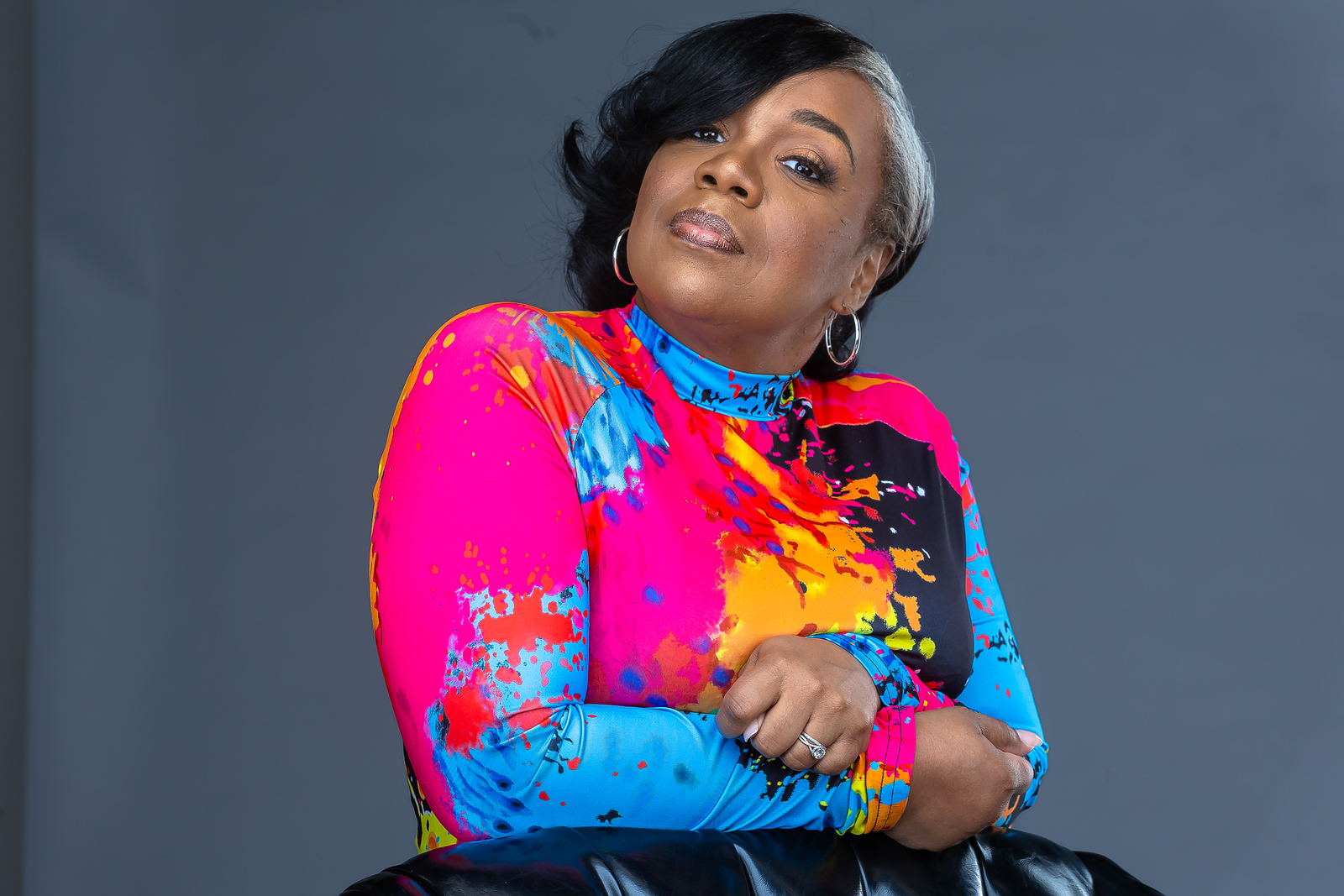 Studio portrait of Marsha in a bright paint-splatter top.